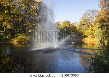 Fountain and rainbow in Riga Canal that flows through Bastion park autumn background with colored leaves (Bastejkalns). Latvia autumn
