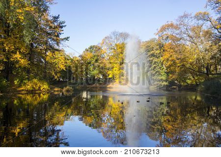 Fountain and rainbow in Riga Canal that flows through Bastion park autumn background with colored leaves (Bastejkalns). Latvia autumn