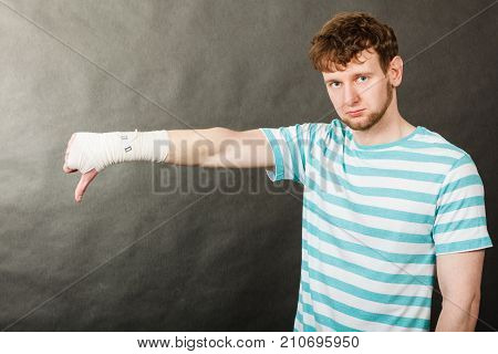 Bad news and information. Medicine aspects. Sad unhappy male with bandaged hand showing thumb down sign symbol.
