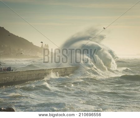A huge ocean wave crashes over a harbor wall at Kalk Bay, Cape Town, South Africa