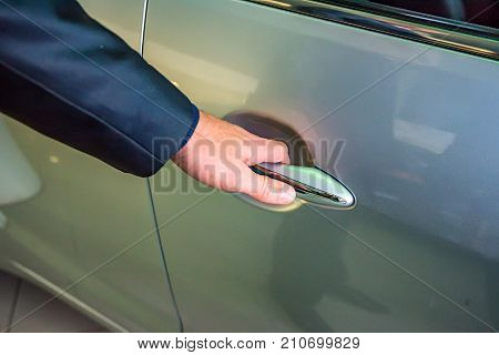 Male hand holding silver doorhandle a white car