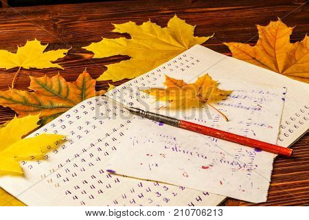 Old School Exercise Book With A Wooden Ink Pen And Yellow Maple Leaves On A Background Of Old Wood .