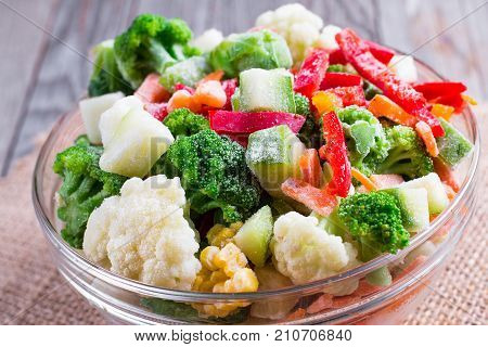 Frozen vegetables in bowl on wooden background