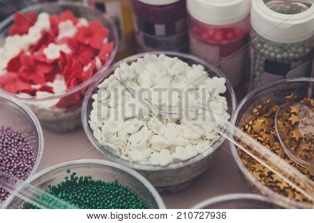 Ice cream treats and toppings sale. Rainbow sprinkles, stars, non pareil and glitter cupcake decorations, white. Closeup in plastic plates with spoons. Confectionery store