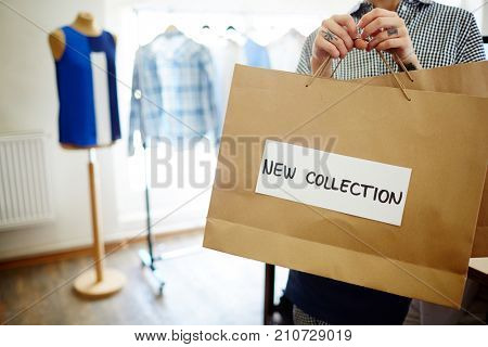 Paperbag with clothes from new author collection held by contemporary fashion designer or tailor