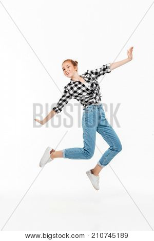 Full length image of carefree ginger woman in shirt and jeans jamping and looking at the camera over white background