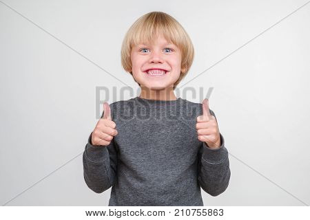 Happy teenager blond with gray eyes smiling widely and showing both hands gesture thumb up. Isolated on white