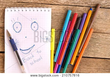 Open white notepad with drawing and inscription BACK TO SCHOOL with colorful felt-tip pens and ball pens on the table