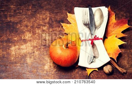 Dinner plate setting top view with Thanksgiving decorations on old wooden table. Seasonal cutlery on Autumn background.