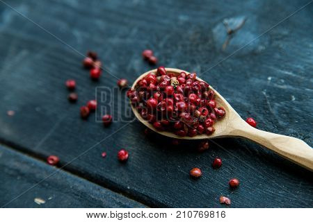 Close up wooden spoon with pink peppercorn on dark background