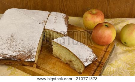piece of apple pie powdered with sugar powder charlotte on a wooden board with whole apples