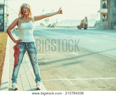 Young teenage style woman with sunglasses standing at the city road with thumbs up handsign.