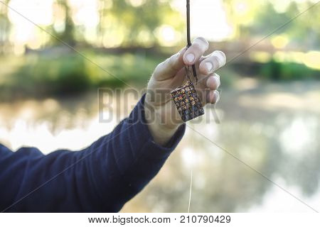 An angler's hand holds a groundbait box with a bait.