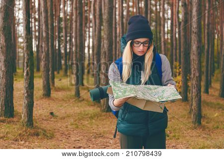 A beautiful young woman with travel map and backpack in pine forest