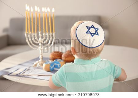 Cute boy sitting near nine-branched menorah on table at home