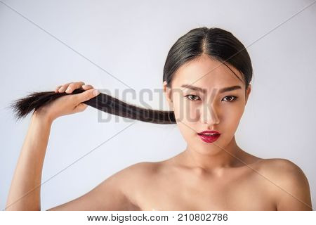 Beauty portrait of young asian woman with her hand pulling her long black hair isolated on white background. Happy beautiful asian tan woman.