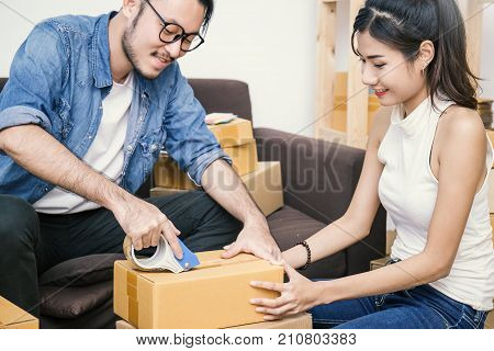 Young asian man and woman taping up a cardboard box in the office SME business relocation and new small business concept SME concept