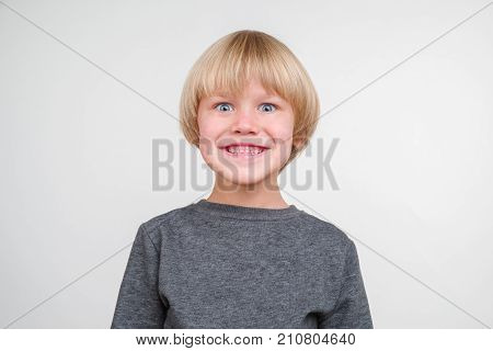 Funny little boy in a gray pullower posing on the camera in studio. Happy smiling child on the gray background. Close-up of little boy.