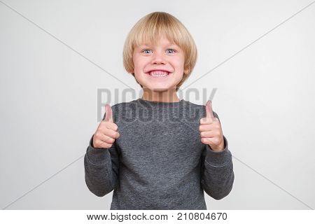 Funny little boy in a gray pullower posing on the camera in studio. Happy smiling child on the gray background. Close-up of little boy.