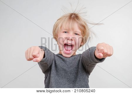 Funny little boy in a gray pullower posing on the camera in studio. Happy smiling child on the gray background. Close-up of little boy.