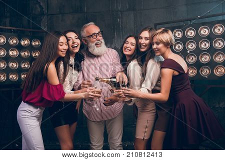 Modern Santa pours champagne into girl's glasses and smile. Happy Christmas day with fun group of attractive girls ad bearded man