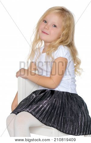 A little girl is sitting on a stool. The concept of a happy childhood. Isolated on white background