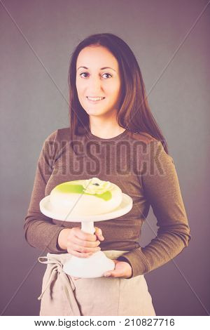 Portrait of young pastre shef with cake on gray background.