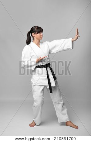 Young woman practicing karate on light background