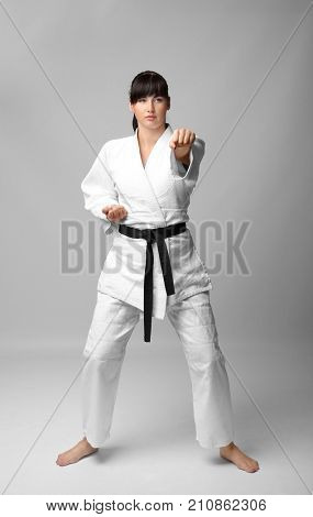 Young woman practicing karate on light background