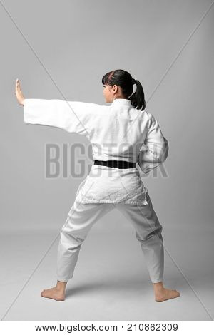 Young woman practicing karate on light background