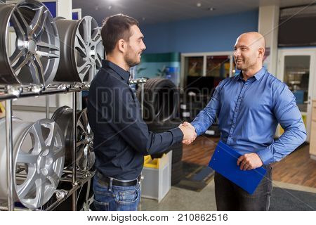 business, partnership and people concept - male customer and salesman shaking hands at car repair service or auto store