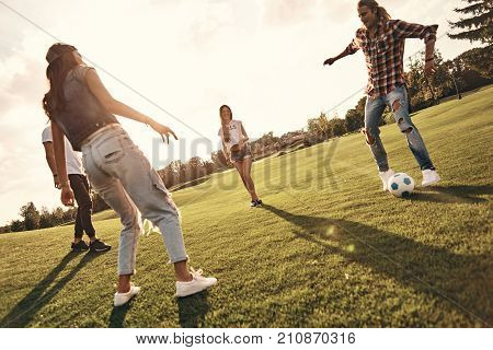 Amazing footwork. Full length of young smiling people in casual wear playing soccer while standing outdoors