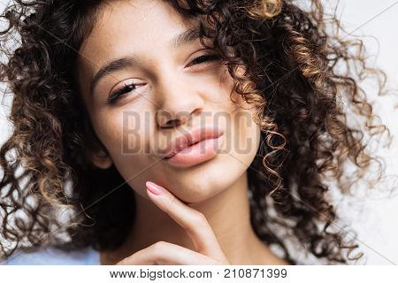 Sensual attractiveness. Charming curly-haired dark-haired woman touching her chin with her finger and pouting while looking at the camera
