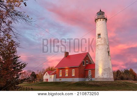 Tawas Point Lighthouse at Sunset in Tawas Michigan. A vivid sunset paints the sky at twilight behind the lighthouse at Tawas Point State Park. A glow reflects from the windows