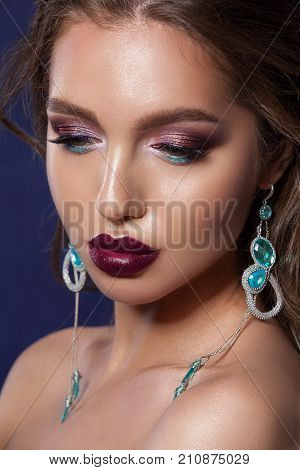 Beauty woman face with beautiful make-up colors. Dark hair beautiful long earrings clear skin beautiful face plump lips. Portrait of a close-up shot in the studio on a blue background.