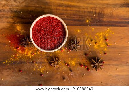 Close up white wooden bowl filled with paprika powder on dark wooden surface covered with anise and turmeric