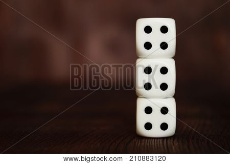 Three white plastic dices column on dark brown wooden board background. Six sides cube with black dots. Unlucky number four - 4. Tetraphobia concept.