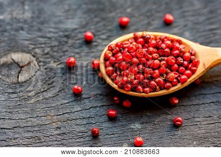 Close up wooden spoon with pink peppercorn on dark background
