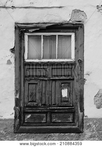 old shabby window in a decaying house with weathered wood and peeling paint set in a flaking concrete wall