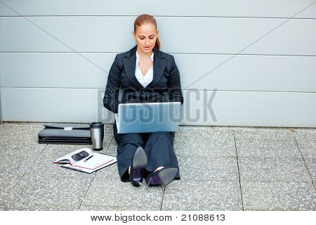 사무실 건물 및 노트북을 사용 하 여 바닥에 앉아 생각에 잠겨있는 현대 비즈니스 우먼