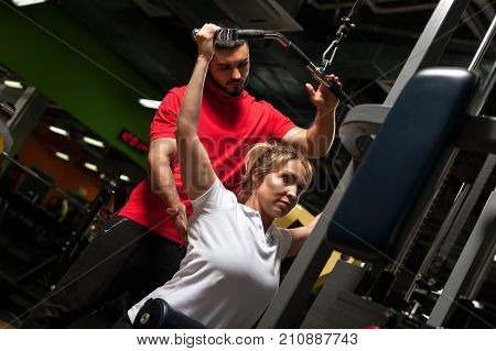 Middle aged blonde woman working out with personal fitness coach. Young male trainer assisting female client in gym. Healthy lifestyle, fitness and sports concept.