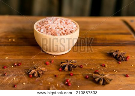 Pink Himalayan salt in a white bowl on wooden surface covered with anise and red peppercorn
