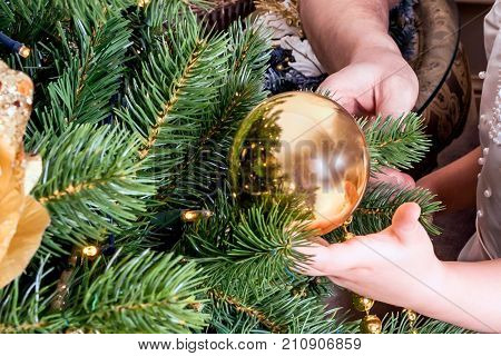 A child and an adult decorate a Christmas tree. A Christmas ball in a child's hand. The symbol of the new 2018 is Yellow Dog. All ornaments should be yellow or gold.