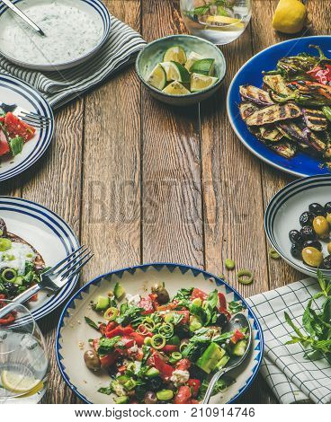 Healthy dinner table setting. Fresh salad, grilled vegetables with yogurt, dill and garlic sauce, pickled olives over wooden background, copy space, selective focus. Clean eating, vegetarian food