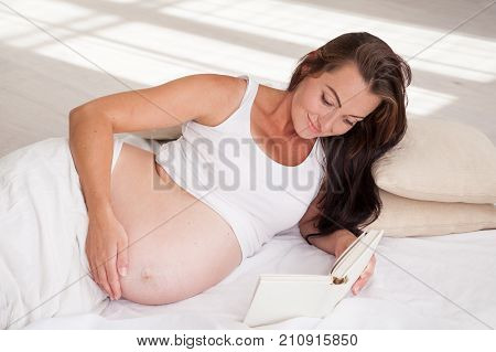 a pregnant woman lies on a bed and reading a book 1