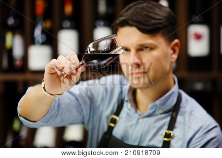 Bokal of red wine on background of male sommelier appreciating color, quality, flavor and sediments of drink. Professional degustation expert in winemaking.