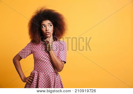 Close-up portrait of retro stylish african thinking woman touching her face, looking aside, isolated on yellow background
