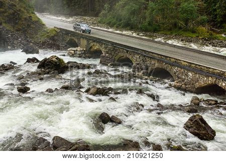 Pickup truck driving on old stone bridge crossing waterfall. Latefoss, Norway.