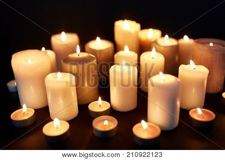 mourning and commemoration concept - candles burning in darkness over black background