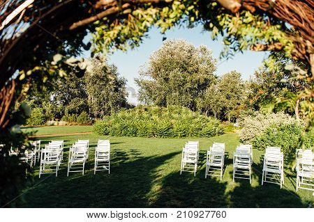 Place for wedding ceremony with white chairs and an arch of living plants